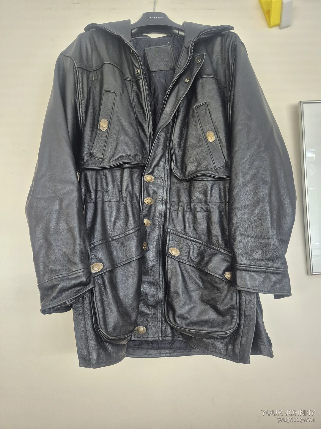 Zwarte vintage jas met capuchon, rits, metalen knopen en zakken op een hanger